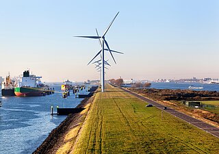 Wind turbines on a dyke, cargo ships in the water and the port of Rotterdam in the background.